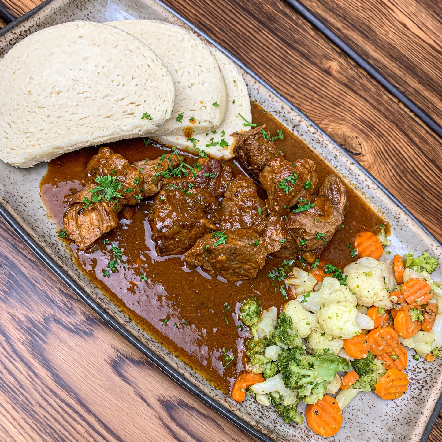 Rindersaftgulasch mit Knödel und Mischgemüse auf Teller